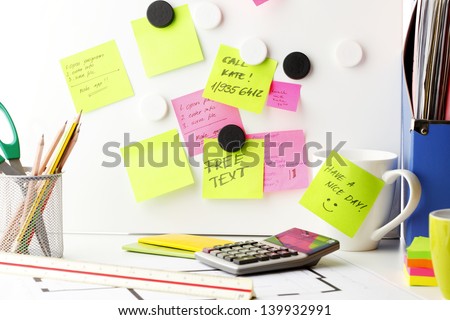 Office work area. Desk with pink and yellow \'Post It\' notes.
