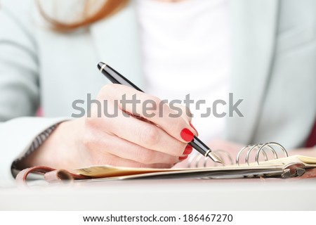 Close-up of businesswoman\'s hand while writing note in diary. Small business.