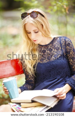 Portrait of attractive female student reading book, while sitting at campus area. Student life.