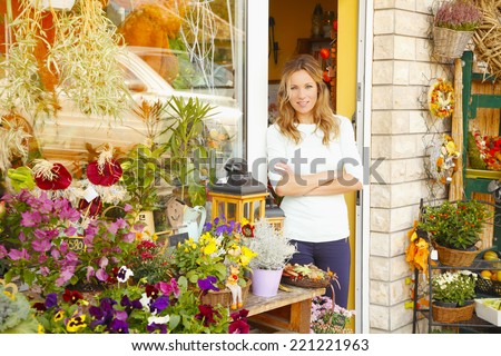 Portrait of smiling flower shop owner standing in front of shop window. Small business.