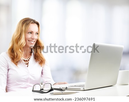 Portrait of middle age business woman with laptop sitting at office and working on project.