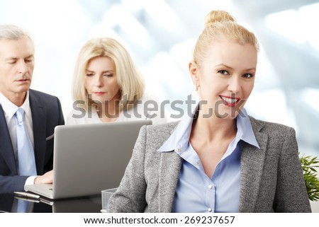 Portrait of executive businesswoman sitting at office while business people working on laptop in background. Teamwork at business meeting.
