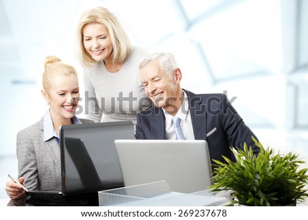 Portrait of businesswoman and businessman sitting in front of computer while sales woman standing in background. Business team working on presentation at office.
