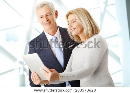 Portrait of middle age businesswoman standing at office and holding hands digital tablet while consulting with senior manager. Teamwork at office.