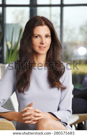 Image of attractive sales woman sitting at office while looking at camera and smiling.