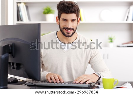 Close-up portrait of handsome bearded graphic designer at workplace. Young creative man sitting in front of computer and checking emails at office. Small business.