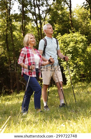 Full length portrait of senior couple enjoying a nordic walk. Active elderly woman and man walking on the forest and smiling.