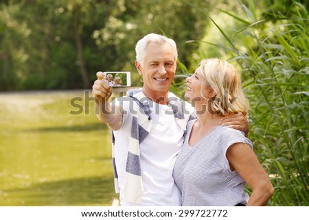 Portrait of happy senior people standing at lakeside while elderly man taking self portrait with his mobile phone.