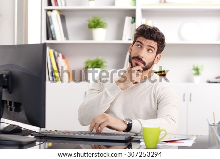 Close-up portrait of young man sitting in front of computer at office while thinking on the problem. Small business.