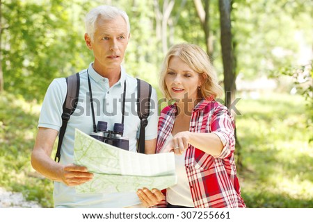 Portrait of senior couple enjoying a sunny day in a forest and looking for the next destination in a map. Elderly man holding hands map while mature woman point on the map.
