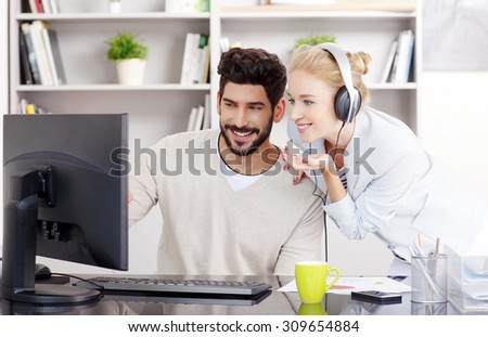 Portrait of creative team working at office and listening music. Young businessman sitting in front of monitor and beautiful businesswoman with headphone standing next to him and share music.