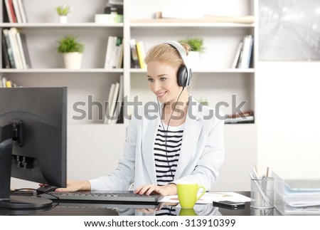 Portrait of smiling businesswoman using headphone and listening music while typing at keyboard in her workplace.