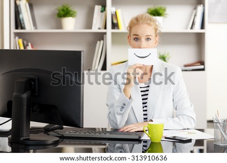 Portrait of young creative female sitting at office in front of computer. Beautiful businesswoman holding a digitally generated card in front of her face.
