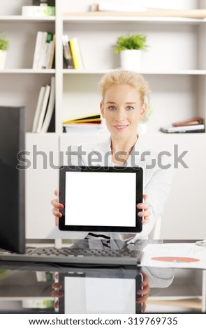 Portrait of young creative woman sitting at desk at office and holding in her hands digital tablet white blank screen.