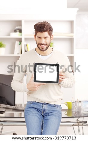 Portrait of young sales assistant standing at workplace. Smiling businessman holding in his hands digital tablet with a blank white screen.