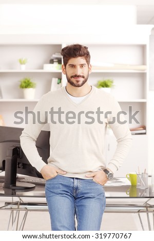 Portrait of young sales man standing at his workplace while looking at camera and smiling. Businessman wearing casual clothing.