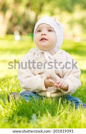 Cute baby in a hat and blouse sitting on the grass