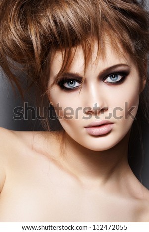 Fashion model with tousled hair, make-up. Portrait of young fashion woman with punk rock hairstyle, dark evening makeup on gray background