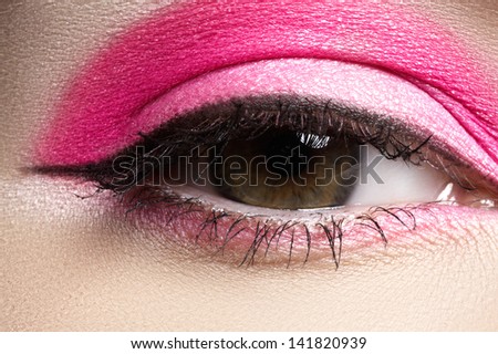 Cosmetics and beauty care. Macro close-up of beautiful green female eye with bright fashion runway make-up. Pink eyeshadows and black eyeliner
