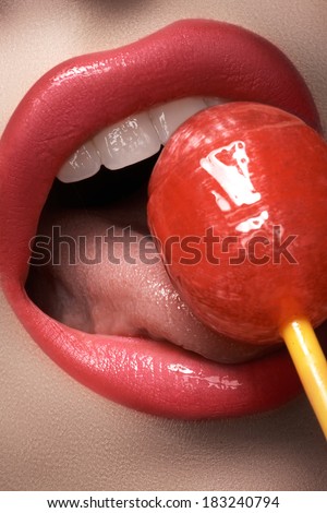 Glamour macro shoot with sexy woman\'s lips with a sweet bonbon. Beautiful bright fashion make-up. Girl licking a strawberry lollipop.