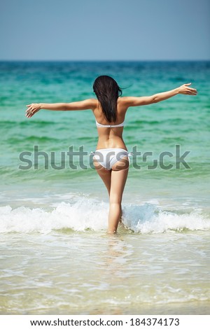 Happy woman in white bikini swimwear open her heart to sun. Vacation, beautiful sea and natural. Tan girl in summer. Perfect body shapes, relaxing soul