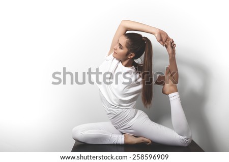 Beautiful young woman in yoga posing on a studio background. Nice sport hairstyle like pony tales. Girl in white clothes for fitness and pilates. Perfect shapes, fit and strong body in asana