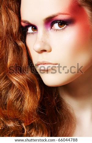 Close-up portrait of beautiful woman model with fantasy fashion eyes make-up and chic long curly red hair.