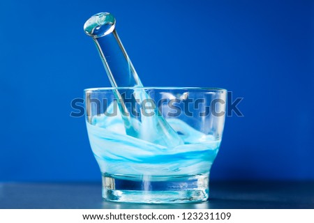 A glass mortar and pestle with a mixture of blue and white compounds. Photographed on a blue background.