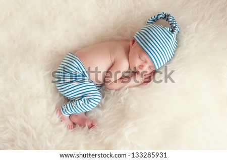 Newborn baby wearing blue and white striped pajamas and sleeping on off white faux fur.
