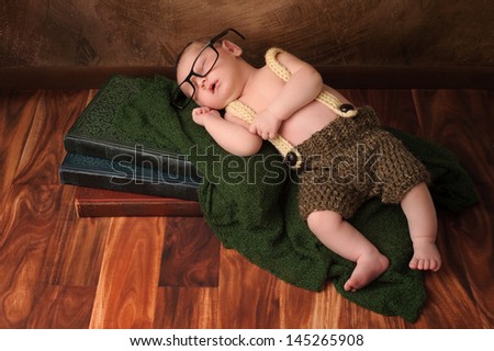 Ten day old newborn baby boy wearing crocheted shorts and suspenders. He has on adult reading glasses and is sleeping on a stack of vintage books.