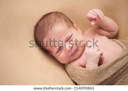 A 3 week old, fussy newborn baby boy. Shot in the studio on a beige blanket.