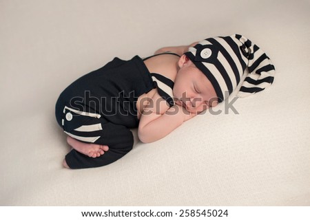 A studio shot of a newborn baby boy sleeping on his stomach, wearing a navy blue and white romper with matching hat.