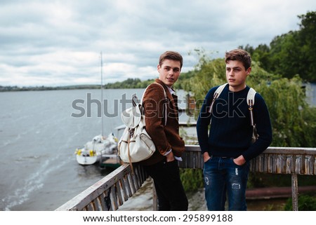 two young guys stand on the pier and one of them turned his head