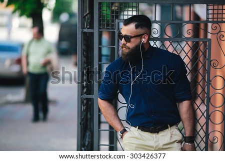 bearded man standing in the street at the bus stop and listen to music
