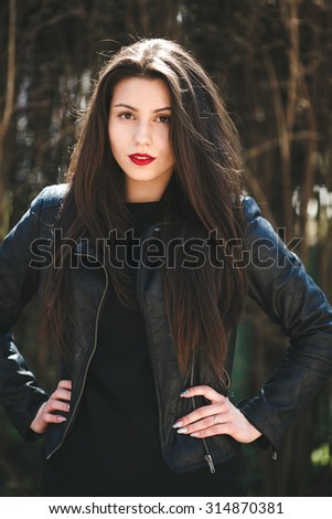 young beautiful girl posing in a black leather jacket in the park