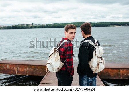 two young guys stand on the pier and one of them turned his head