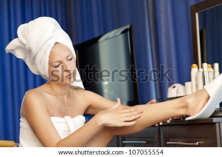 Young woman with cosmetic lotion in a bedroom. Concept body care. She is applying moisturizer cream on her slim legs