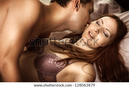Beautiful sexy couple of  lovers. Young man kissing woman in darkness bedroom on bed