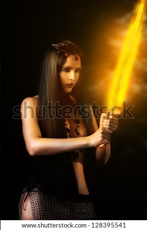 Young sexy woman warrior holding fire sword in hands with long healthy black hair.