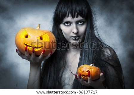 Halloween makeup. Sexy woman - Witch with long black hair and two pumpkins in hands smiling and look to shot