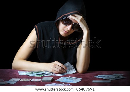 Poker face. Person in sun glasses and hood playing poker at the table with cards and money