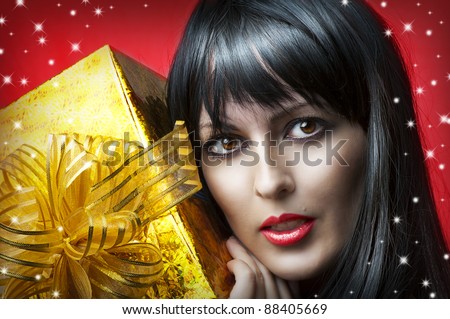Glamour portrait of beauty woman with gold christmas gift box with ribbon on red background