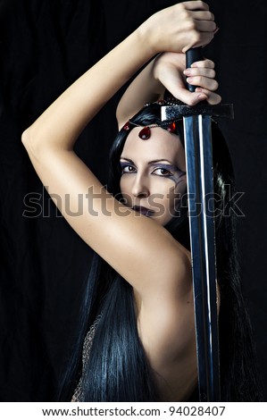 Young sexy woman warrior holding sword in hands with long healthy black hair.