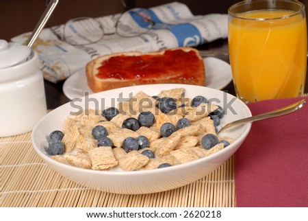 Bowl of wheat cereal with blueberries, toast, orange juice and newspaper