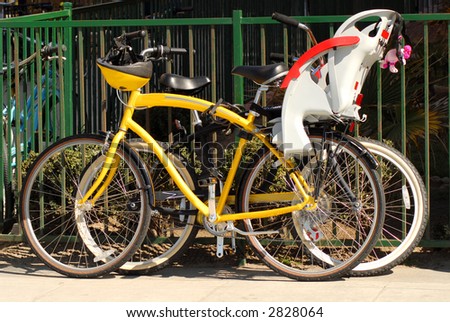 Two bicycles resting against a fence on the sidewalk