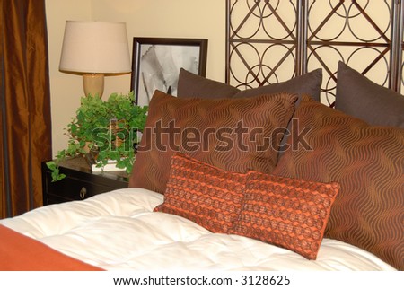 Comfortable bed with earth tone pillows and nightstand