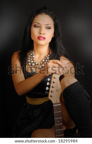 Attractive hispanic female rocker with guitar and dramatic lighting