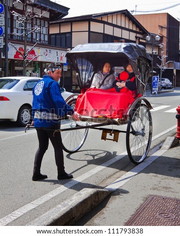 HIDA TAKAYAMA, JAPAN - MARCH 26: An unidentified man and his traditional rickshaw with unidentified tourists near the old preservation town area on March 26, 2012 in Hida Takayama, Japan.