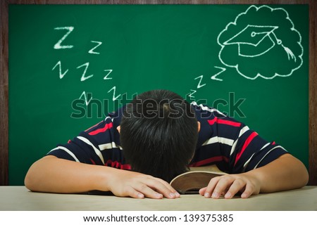 Asian boy\'s sleeping on a book and dreaming of graduation
