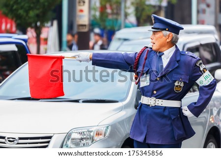 KOBE, JAPAN - NOVEMBER 17: Security Guard in Kobe, Japan on November 17, 2013. Unidentified security guard raises a red flag at a traffic lights for people to cross the street at Motomachi street
